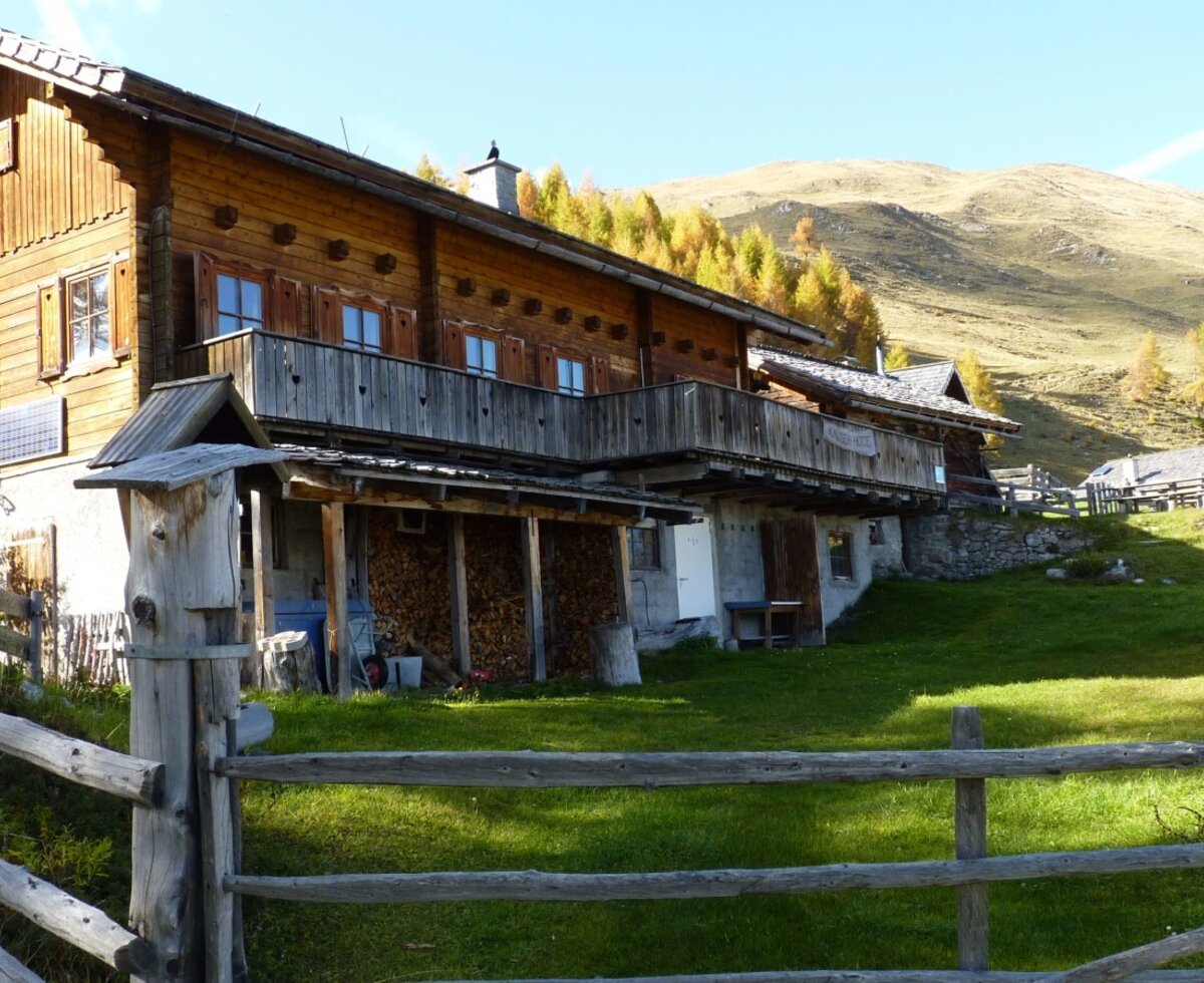 Die Massivholzalmhütte mit ihren Balkonen und der umgebenden Gebirgslandschaft.