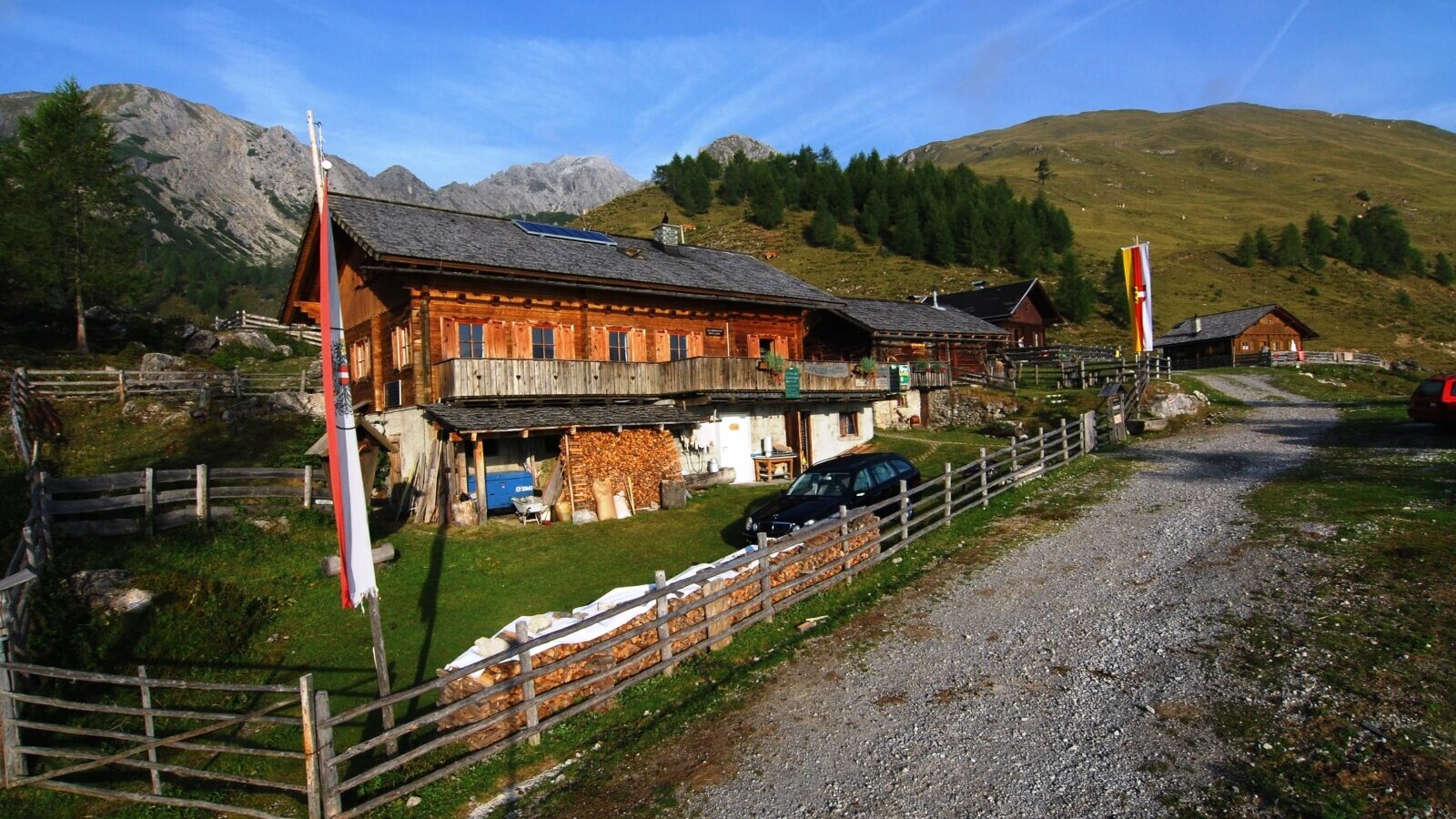 Die Alm in traditioneller Holzbauweise mit Balkon und Zufahrt inmitten der Gebirgslandschaft.