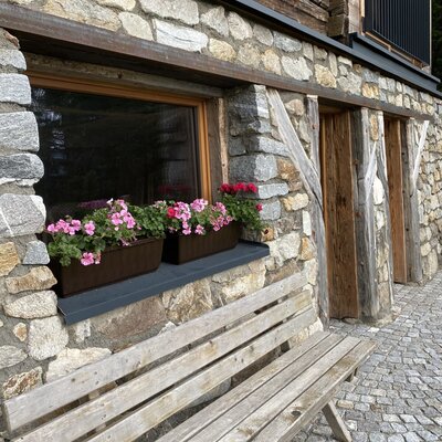 Ein einladender Sitzbereich vor der Almhütte mit einer rustikalen Holzbank und farbenfrohen Blumenkästen am Fenster.