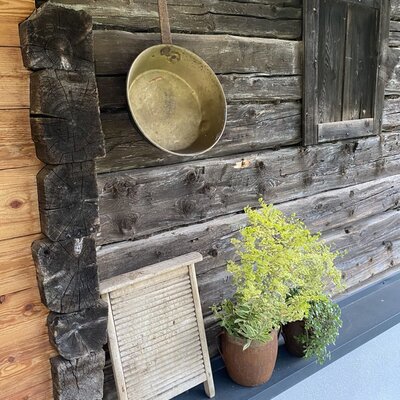 Liebevoll dekorierte Holzwand der Almhütte mit urigen Details wie einer alten Messingpfanne, einem Waschbrett und frischen Topfpflanzen.