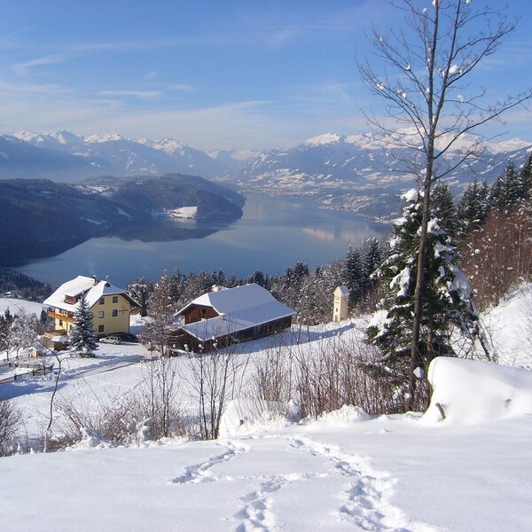 Der Bauernhof in verschneiter Landschaft mit Blick auf den Millstättersee und die umliegenden Berge.