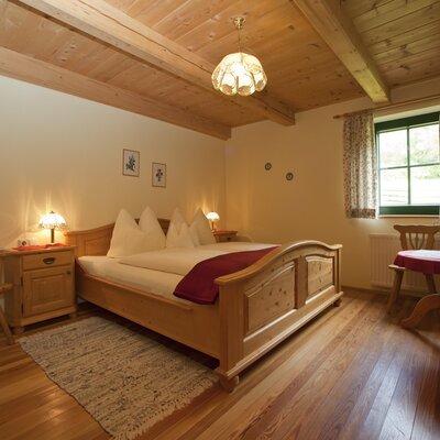 Schlafzimmer im Bauernhof mit Doppelbett, Holzmöbeln, Holzboden und Holzdecke mit Sichtbalken.
