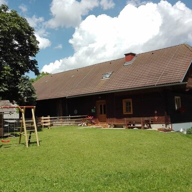 Das Ferienhaus Morgensonne mit Balkon, umgeben von einer Rasenfläche und einem Kinderspielplatz mit Schaukeln und Spielhaus.