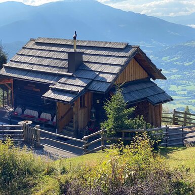 Die Alm mit Außenterrasse und Sitzgelegenheiten mit Blick auf das Tal und die Berge.