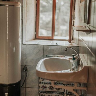 Badezimmer in der Alm mit Waschbecken, Warmwasserboiler und Fenster.