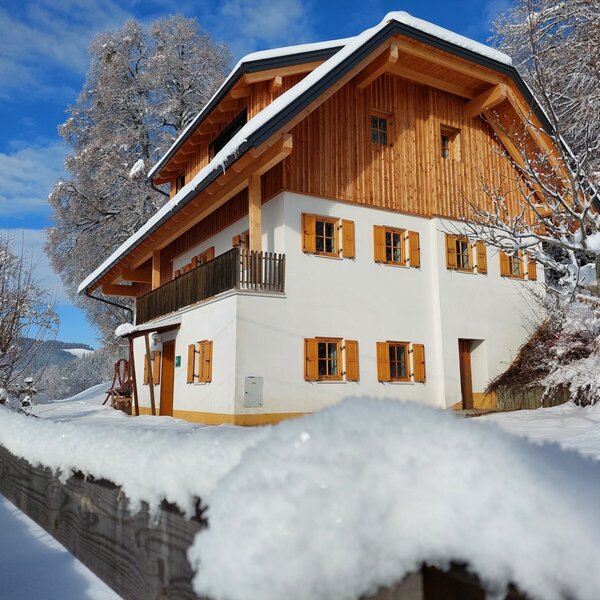 Die Alm Kreinzhuabn im Winter, mit schneebedecktem Dach, Holzfassade, weißen Wänden und einem Balkon.