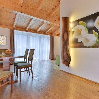 Essbereich im Bauernhof mit Holzboden, Holzbalkendecke, Esstisch, Stühlen, Fernseher, großen Fenstern und einem beleuchteten Wandbild.