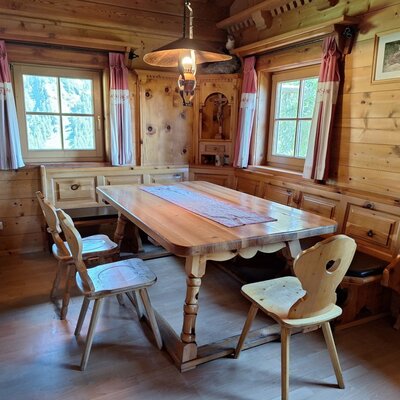 Ein gemütlicher Essbereich in der Alm mit einem rustikalen Holztisch, einer einladenden Eckbank und traditioneller Holzvertäfelung.
