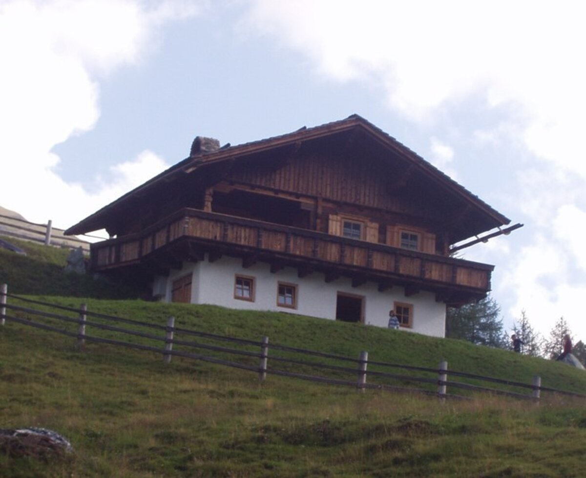 Eine einladende, urige Alm in Hanglage mit einem traditionellen Holzbalkon.