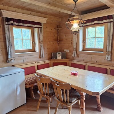 Die gemütliche Essecke der Alm mit einer traditionellen Eckbank aus Holz, einem großen Esstisch und warmem Licht.