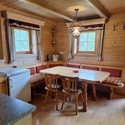 Ein gemütlicher Essbereich in der Alm mit einer rustikalen Eckbank aus Holz, einem großen Esstisch und warmer Beleuchtung.