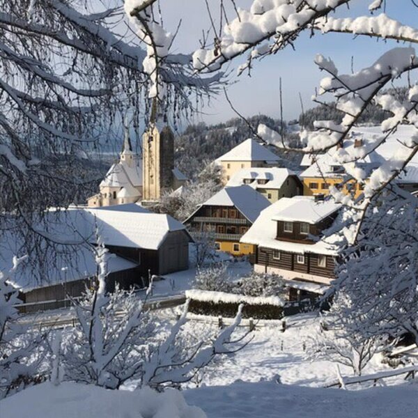 Winterliche Dorfansicht mit schneebedeckten Häusern und einer Kirche in der Umgebung des Bauernhofes.