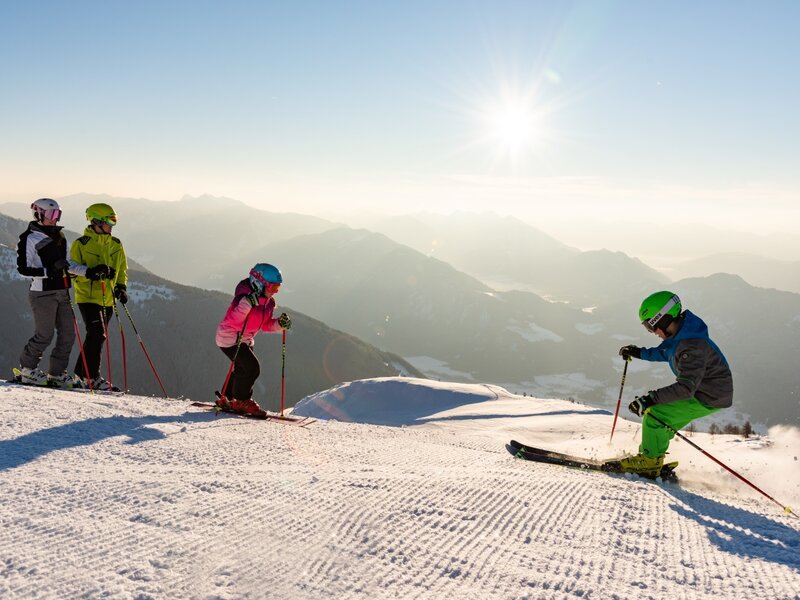 Skifahrer auf einer sonnigen Skipiste mit Blick auf die umliegende Bergwelt, eine Aktivität für Gäste des Bauernhofs.