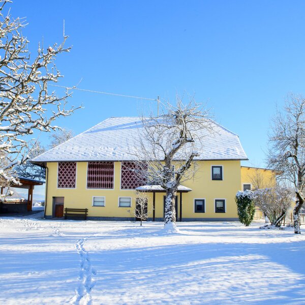 Außenansicht des Bauernhofs mit schneebedecktem Dach und Winterlandschaft unter blauem Himmel.