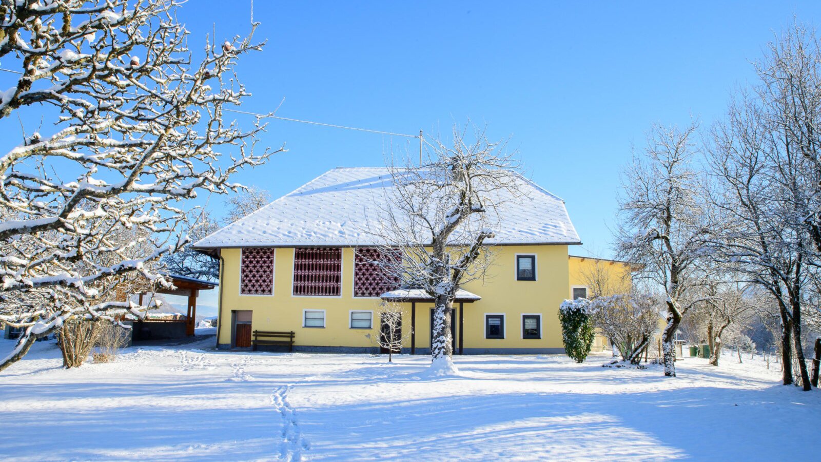 Außenansicht des Bauernhofs mit schneebedecktem Dach und Winterlandschaft unter blauem Himmel.