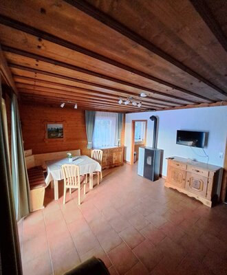Ess- und Wohnbereich der Langhanshütte mit Holztisch, Eckbank, Kaminofen und TV.