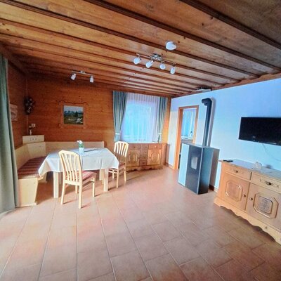 Wohn- und Essbereich mit Esstisch, Eckbank, Fliesenboden, Kaminofen und Fernseher.