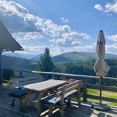 Die Terrasse der Alm mit Holztisch und Sitzbänken und Blick auf die umliegende Berglandschaft.