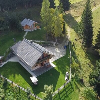 Der Platz aus der Vogelperspektive, mit dem Haupthaus, einem Nebengebäude und eingezäuntem Garten, eingebettet in grüne Wiesen und Wälder.