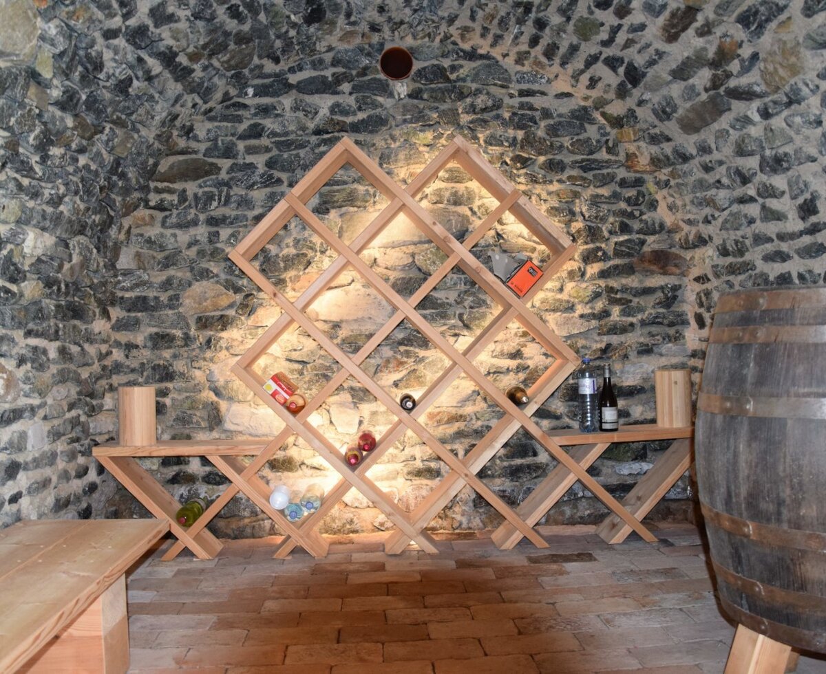 Der Weinkeller der Alm mit Steinmauern, Gewölbedecke, Ziegelboden, einer Holzbank, einem Weinregal und einem Holzfass.