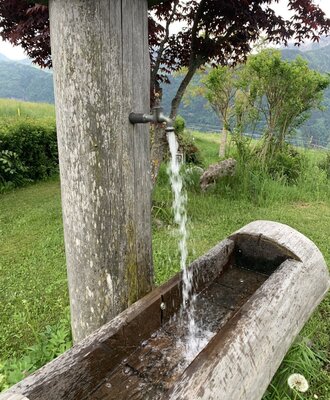 Hölzerner Brunnen mit fließendem Bergquellwasser auf dem Guggenberg s Bauernhofs.