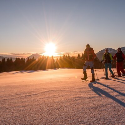 Schneeschuhwanderer am Guggenberg erkunden die verschneite Landschaft bei Sonnenuntergang, eine Aktivität, die Gäste vom Bauernhof aus unternehmen können.