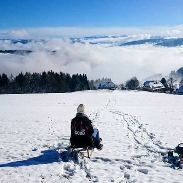 Die verschneite Landschaft des Bauernhofs mit Blick auf die Karawanken und nebelverhangene Täler, ideal zum Rodeln.