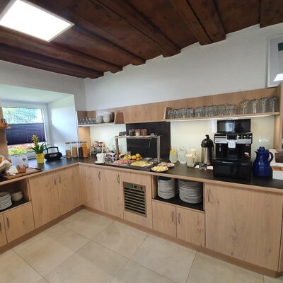 Das Frühstücksbuffet im Bauernhof bietet eine Auswahl an Brot, Aufschnitt, Müsli und Getränken, inklusive einer Kaffeemaschine.