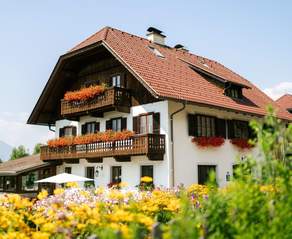 Außenansicht des Bauernhofs mit blumengeschmückten Balkonen, einem farbenfrohen Garten und Bergblick.