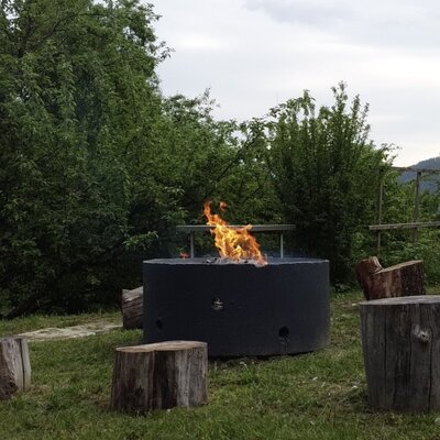 Die Feuerstelle im Freien des Bauernhofs mit lodernden Flammen und Baumstumpf-Sitzen.