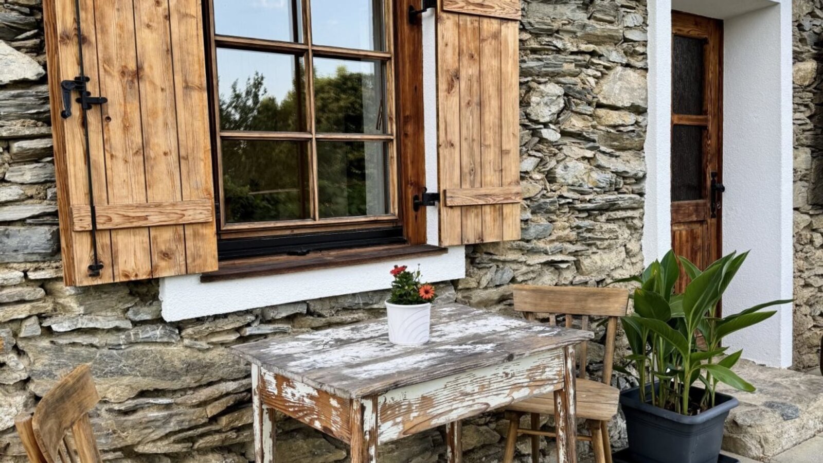 Außenbereich des Bauernhofs mit Steinfassade, Holzfensterläden und Sitzgelegenheiten.