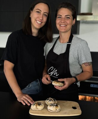 Zwei Personen in der Bauernhofküche mit frisch gebackenen Brötchen.