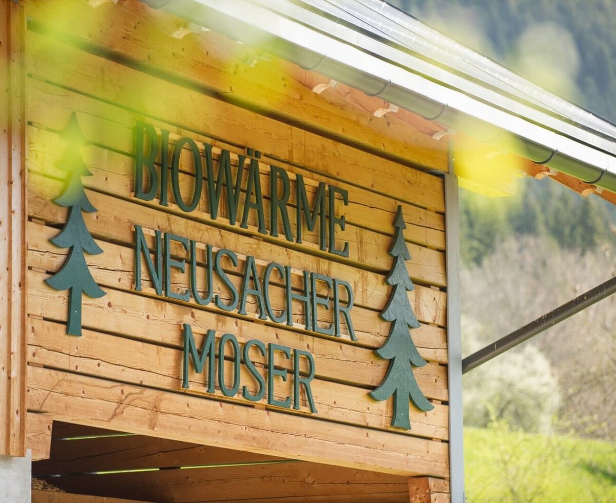 Das Schild "BIOWÄRME NEUSACHER MOSER" an der Holzfassade des Bauernhofs.