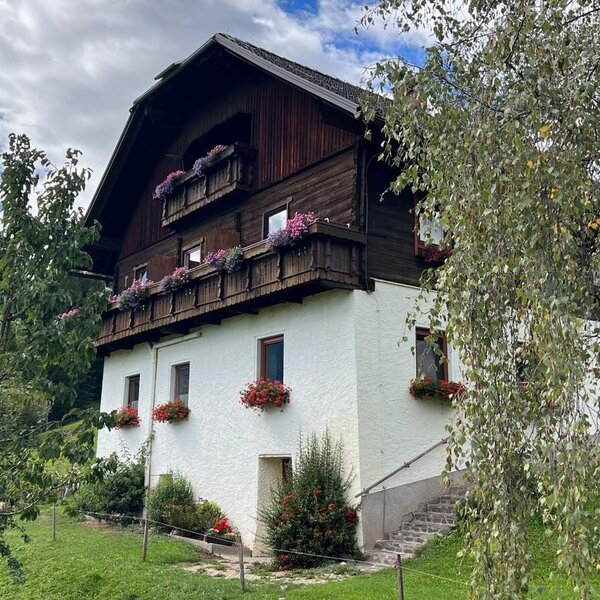 Der einladende Bauernhof mit blumengeschmückten Holzbalkonen und einem weitläufigen, grünen Garten.