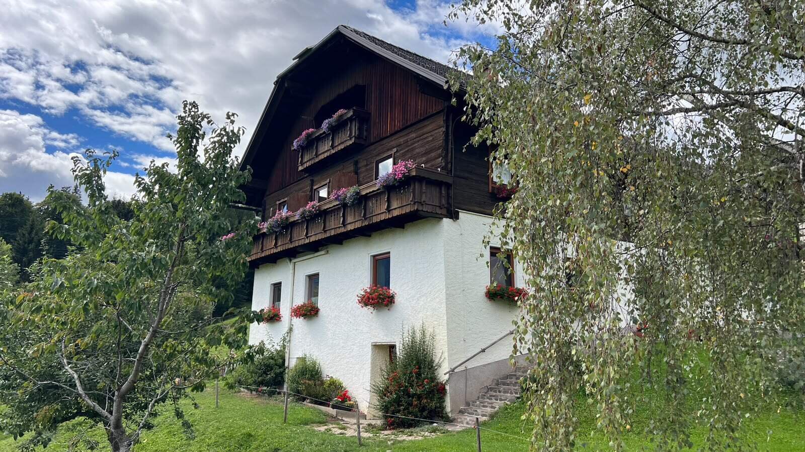 Der einladende Bauernhof mit blumengeschmückten Holzbalkonen und einem weitläufigen, grünen Garten.