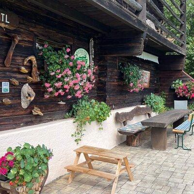 Die einladende Terrasse des Bauernhofs mit rustikalen Holzbänken und farbenfrohem Blumenschmuck.