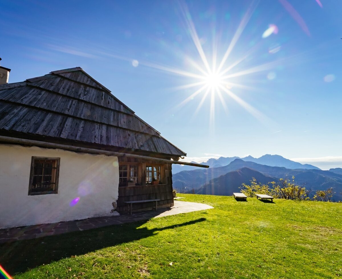 Der Hof mit grünem Rasen, Holzbänken und Blick auf die Berge.