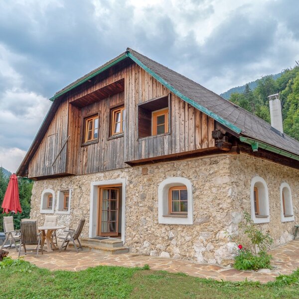 Die Alm mit Steinfassade und Holzverkleidung verfügt über eine Terrasse mit Sitzgelegenheiten und einem Hot Tub, umgeben von der Berglandschaft.