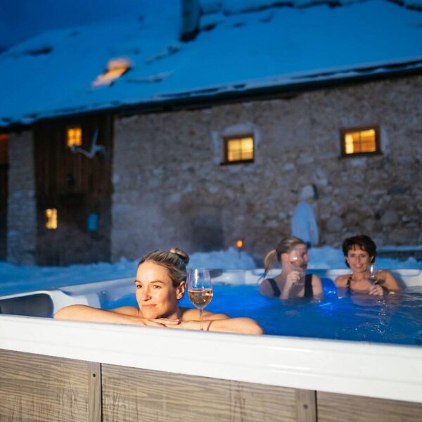Außen-Whirlpool mit Gästen und Getränken auf der verschneiten Alm bei Nacht.