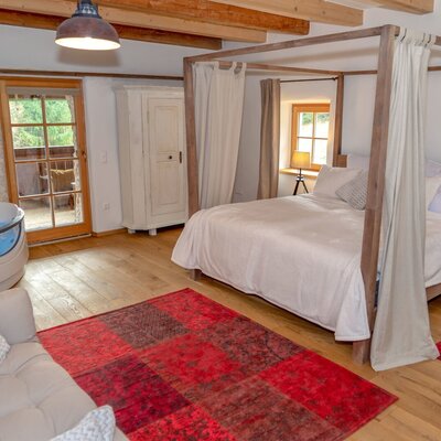 Schlafzimmer in der Alm mit Himmelbett, freistehender Badewanne, Sofa, Kleiderschrank und Zugang zum Außenbereich.