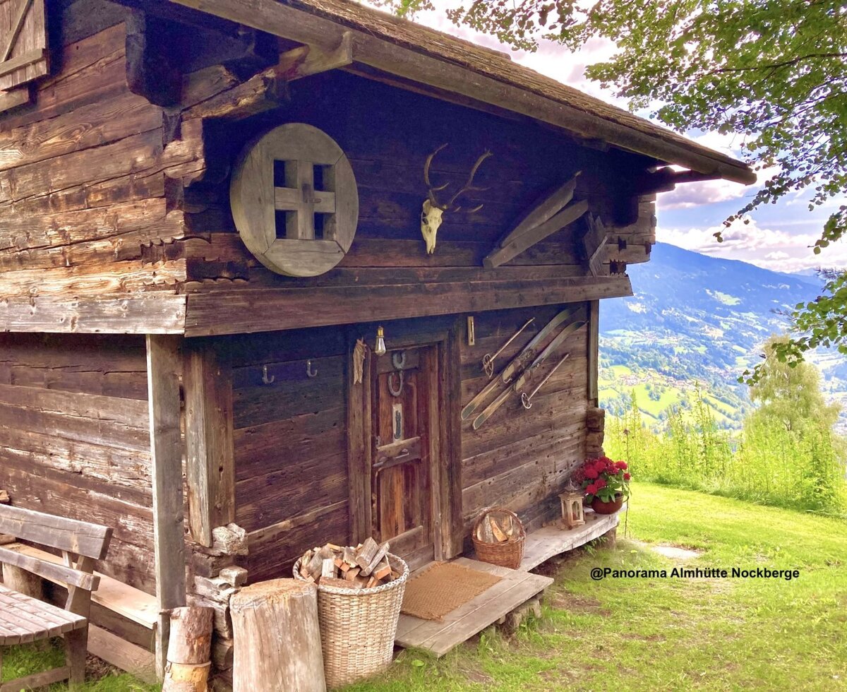 Die rustikale Holzfassade der Almhütte mit traditionellen Dekorationen und Panoramablick Berglandschaft und ins Tal.