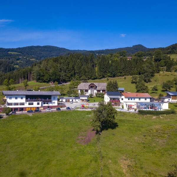 Die Ap­par­te­ments mit Außenpool, Spielplatz und Parkplätzen, umgeben von grünen Wiesen und Wäldern.