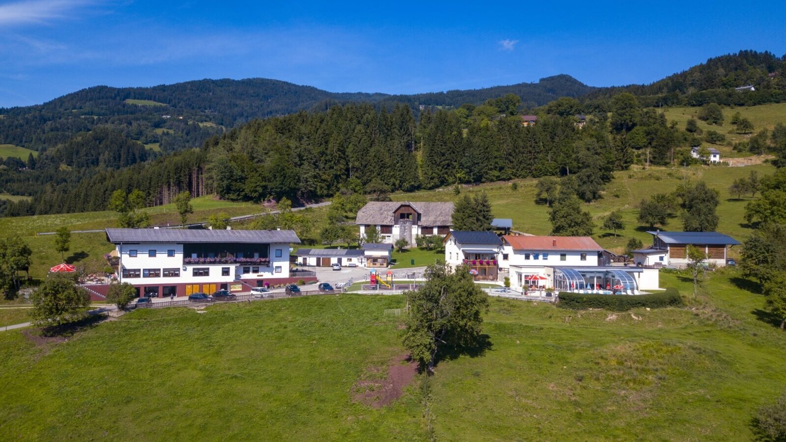 Die Ap­par­te­ments mit Außenpool, Spielplatz und Parkplätzen, umgeben von grünen Wiesen und Wäldern.