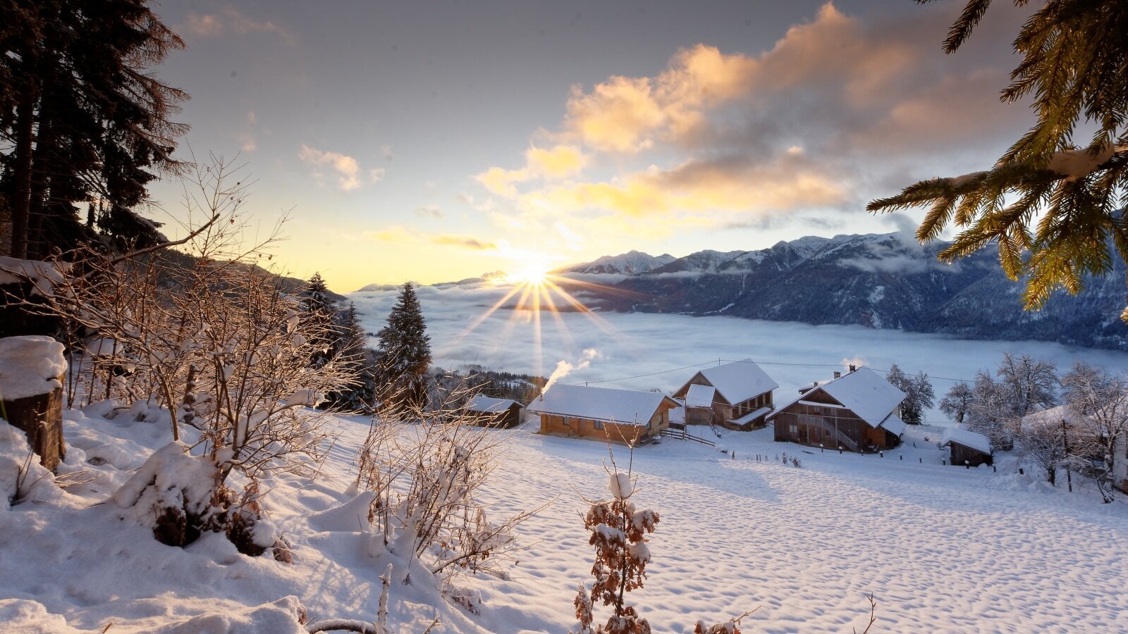 Der Bauernhof in einer verschneiten Winterlandschaft mit Sonnenaufgang über dem Tal und den Bergen.