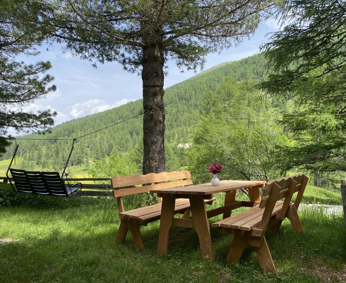 Der Außenbereich der Alm bietet einen Holztisch mit Bänken, eine Schaukel und Blick auf die Berglandschaft.