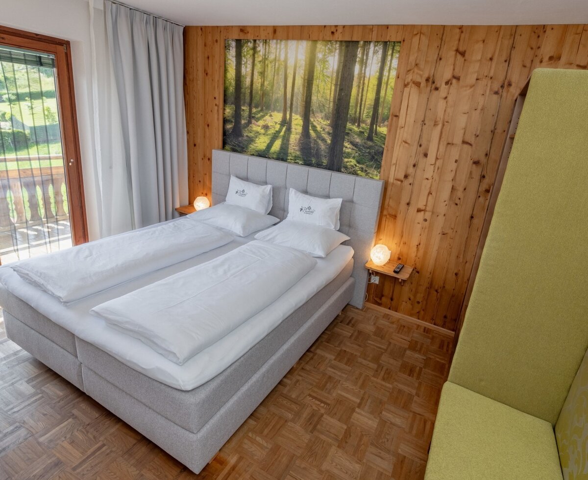 Schlafzimmer im Bauernhof mit Doppelbett, Holzwandverkleidung, einem großen Waldbild, einem grünen Sitzbereich und direktem Zugang zum Balkon.