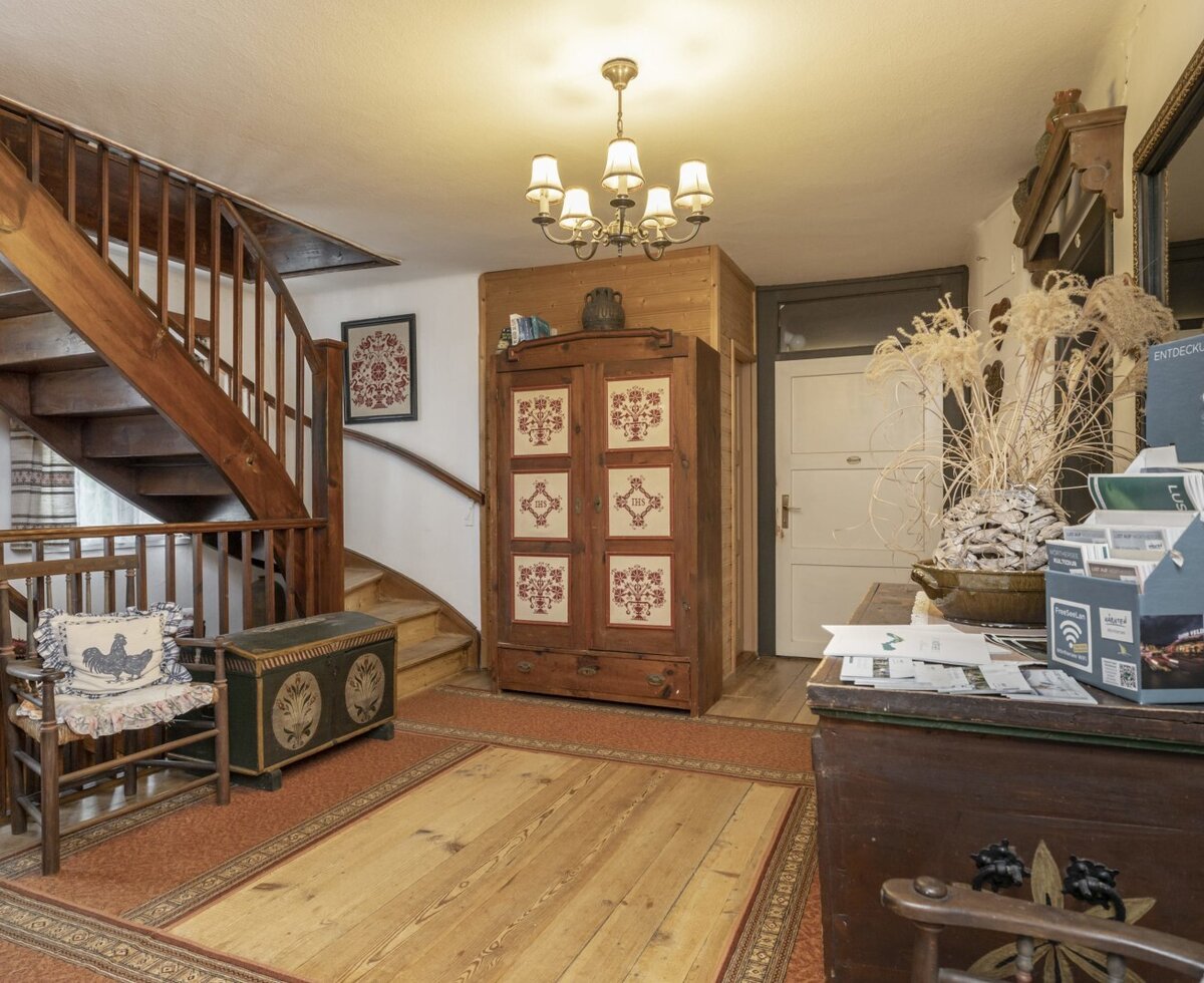 Der Eingangsbereich des Bauernhofs mit einer Holztreppe, traditionellen Vollholzmöbeln und ausliegendem Informationsmaterial.