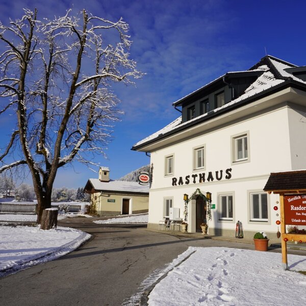 Der Rasdorferhof Bauernhof im Winter mit verschneiter Umgebung, dem Gebäudeeingang und einem Willkommensschild.