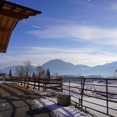 Der Bauernhof im Winter mit schneebedeckten Feldern und Bergblick.