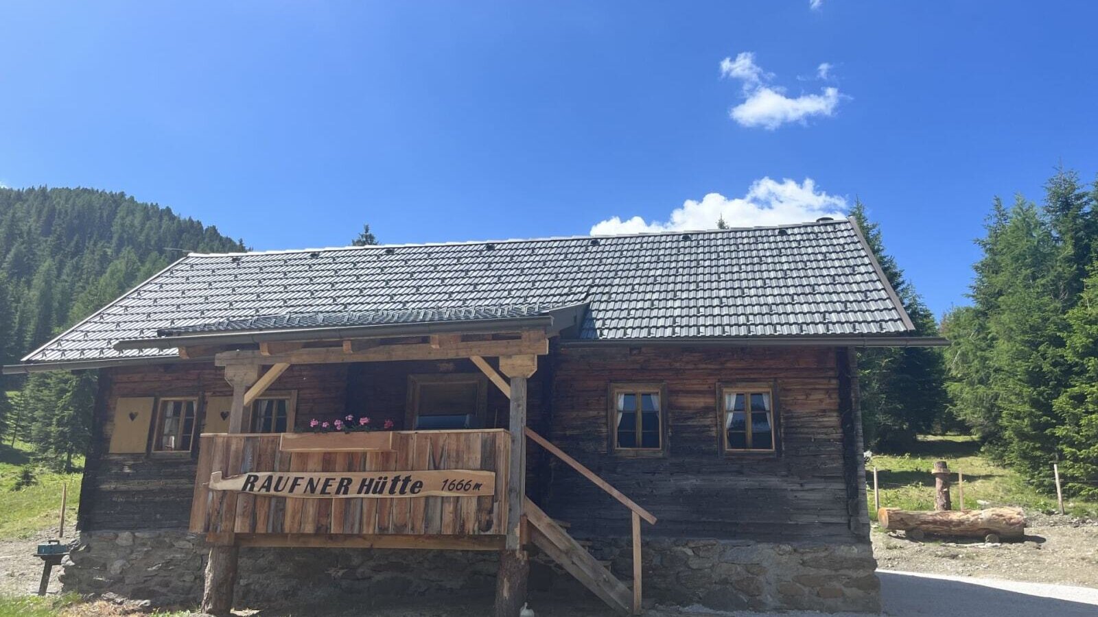 Eine urige Alm auf 1666 Metern Höhe mit einer gemütlichen Holzterrasse unter strahlend blauem Himmel.